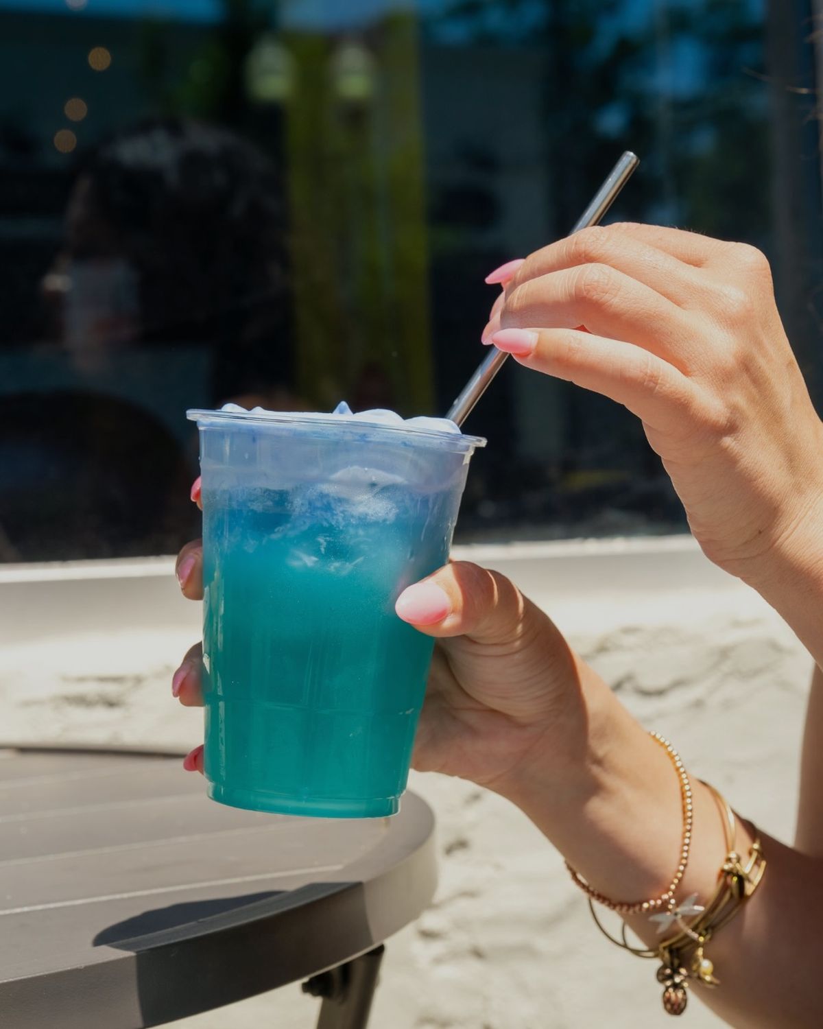 A blue iced drink with a metal straw on the patio table